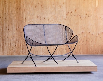 May include: A black metal bench with a wire mesh seat and back. The bench is on a wooden platform.