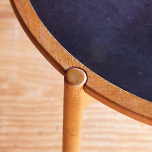 May include: A round wooden table with a black top and a single wooden leg visible. The table top is made of wood with a dark stain and the leg is a solid piece of wood.
