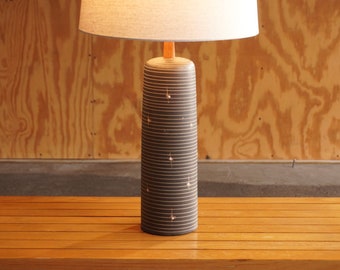 May include: A ceramic table lamp with a white lampshade and a black and white striped base. The base has a subtle pattern of white dots.