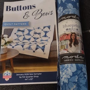May include: A Buttons & Bows quilt pattern booklet by Fat Quarter Shop for a 44" x 53" quilt, displayed next to a roll of blue floral fabric from the Moda Blueprint collection by Camille Roskelley, featuring a photo of the designer.