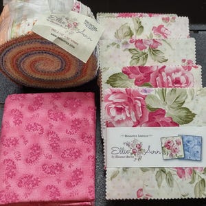 May include: A fabric jelly roll and a stack of fabric squares from the Ellie Ann by Eleanor Burns collection by Benartex. The jelly roll label reads (40) 2-1/2 inch x 42 inch strips. The fabric features pink floral patterns on cream backgrounds.