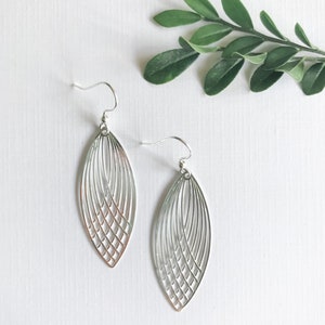 May include: A pair of silver earrings featuring a geometric leaf design. The earrings are made of metal and have a delicate, intricate pattern.