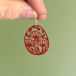 May include: Red dangle earrings with a floral design. The earrings are shaped like an oval and feature a delicate floral pattern.