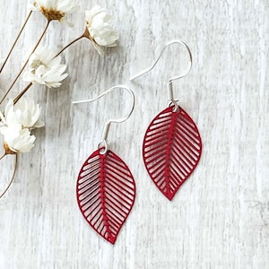 May include: A pair of red leaf-shaped earrings with a delicate, intricate design. The earrings are made of metal and have a silver hook closure.