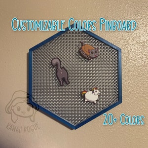 May include: A hexagonal pinboard with a blue frame and a silver mesh surface. The pinboard has three pins with cartoon images of a cat, a unicorn, and a cat with the text "PURE-ITO". The text "CUSTOMIZABLE COLORS PINBOARD" is at the top of the image and the text "20+ COLORS" is at the bottom of the image.