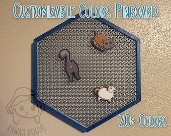 May include: A hexagonal pinboard with a blue frame and a silver mesh surface. The pinboard has three pins with cartoon images of a cat, a unicorn, and a cat with the text "PURE-ITO". The text "CUSTOMIZABLE COLORS PINBOARD" is at the top of the image and the text "20+ COLORS" is at the bottom of the image.