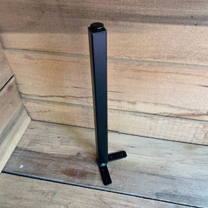May include: Black metal table leg with a square top and a T-shaped base. The leg is about 18 inches tall.