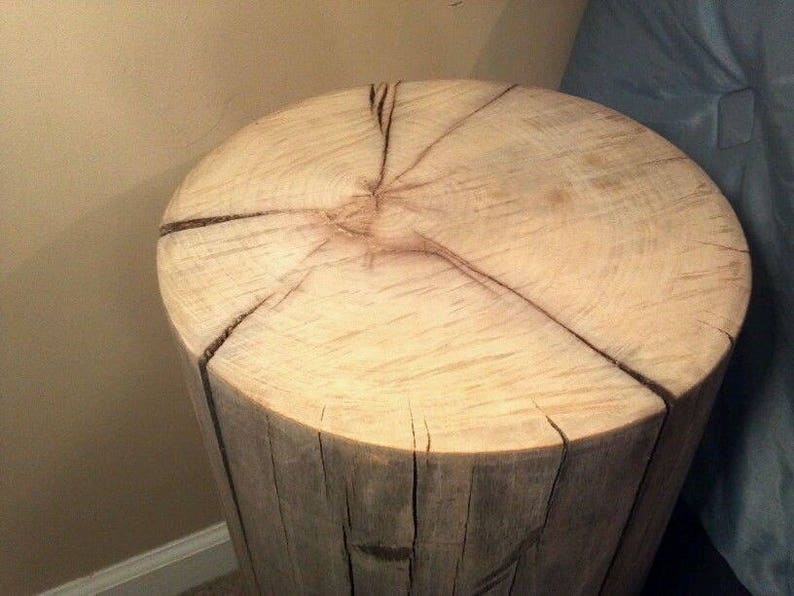 May include: A natural wood stump side table with a light brown finish and a circular top. The top has a natural wood grain pattern and several cracks.