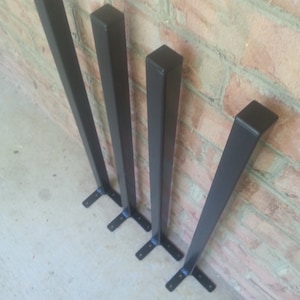 May include: Four black metal table legs of varying heights, arranged in order of size. The legs have a square profile and a flat base.