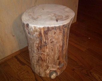 Può includere: Uno sgabello rustico in legno fatto da un tronco d'albero. Lo sgabello ha una finitura in legno naturale e una superficie ruvida e testurizzata.