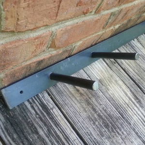 May include: A black metal shelf bracket with three black metal arms extending out. The bracket is mounted to a brick wall and the arms are over a wooden surface.