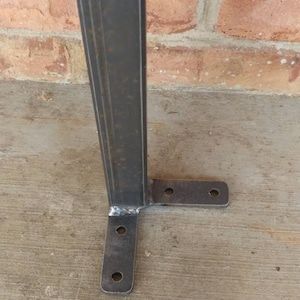 May include: A metal support leg with a rectangular base and four holes. The leg is made of dark gray metal and has a welded seam.