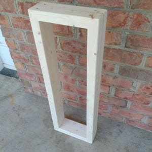 May include: A simple, unfinished wooden frame with a rectangular opening. The frame is made of pine wood and has a natural wood color.