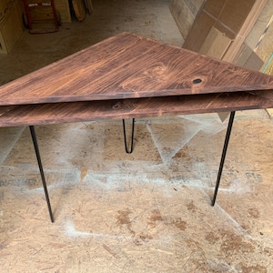 May include: A dark brown triangular table with a shelf and black hairpin legs. The table is made of wood and has a rustic finish.