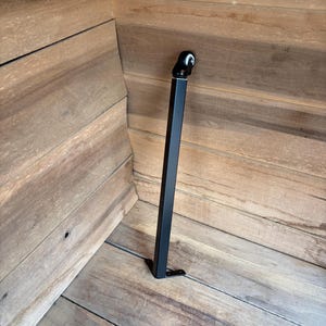May include: A black metal support leg with a swivel head and a foot, designed for furniture or similar applications. The leg is rectangular and stands upright against a wooden surface.