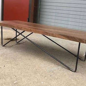 Puede incluir: Un banco de madera rectangular largo con una mancha marrón oscura. El banco tiene un diseño simple y moderno con un marco de metal negro.