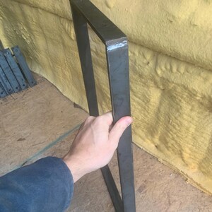 May include: A black metal table leg with welded seams. The leg is rectangular in shape and has a square profile.