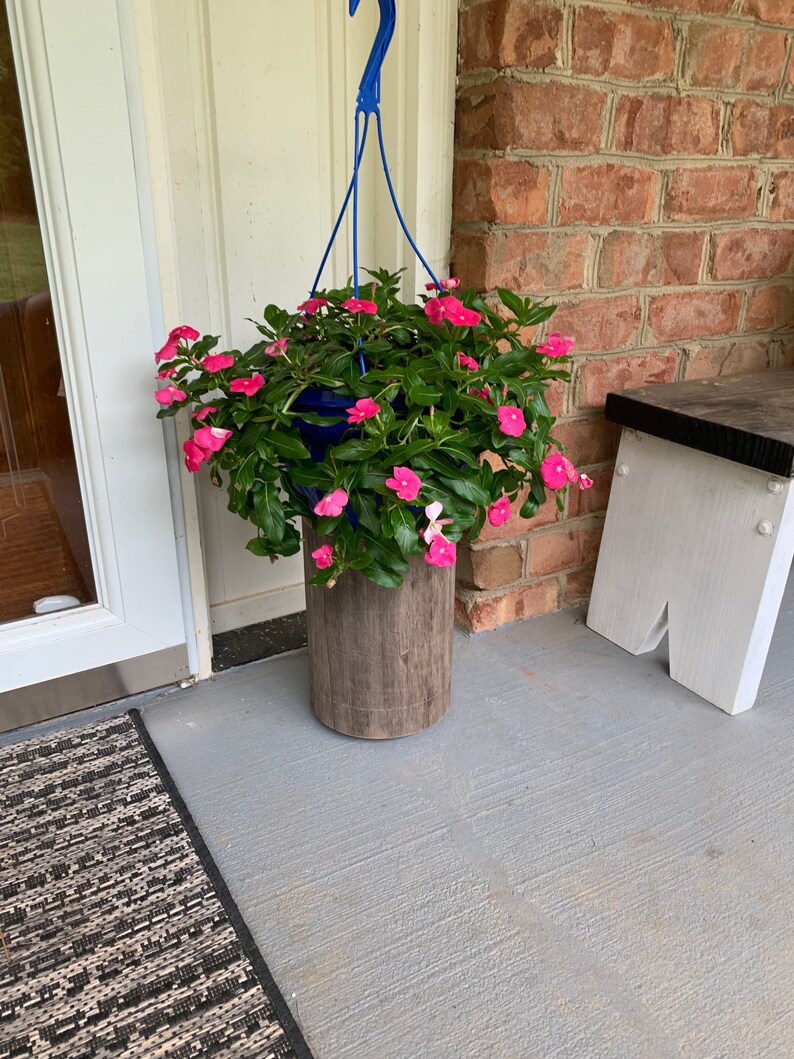 May include: A hanging planter with pink flowers and green leaves. The planter is made of wood and has a blue metal hanger.