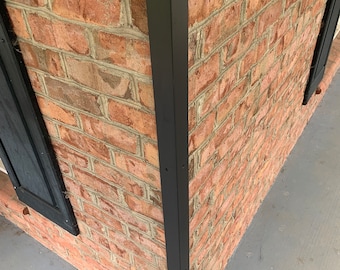 May include: Close-up of a brick wall with a black metal corner trim. The trim has several evenly spaced holes along its length.