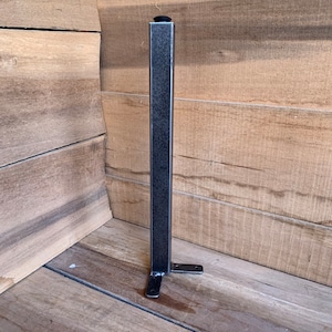 May include: A black metal table leg with a square base and a black rubber foot. The leg is attached to a metal plate with two holes.