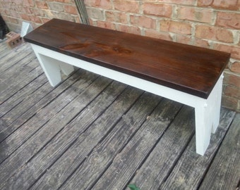May include: A wooden bench with a dark brown stained top and white painted legs. The bench is sitting on a wooden deck.