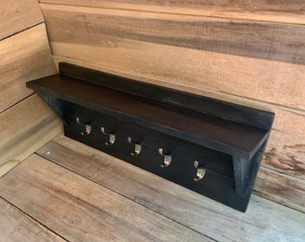 May include: A dark stained wooden wall mounted shelf with five metal hooks. The shelf has a small ledge on top.