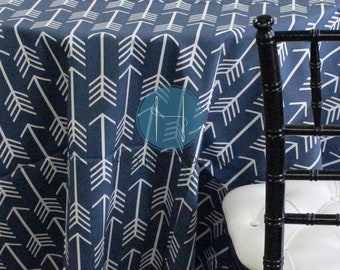 May include: A navy blue tablecloth with a white arrow pattern. The tablecloth is draped over a table and a black chair is in the foreground.