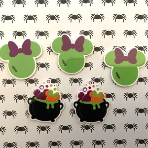 Puede incluir: Cuatro parches termoadhesivos con temática de Halloween. Dos parches verdes presentan un personaje parecido a Mickey Mouse con un lazo morado y detalles cosidos. Dos parches negros presentan un caldero con una poción verde, naranja y morada y burbujas.