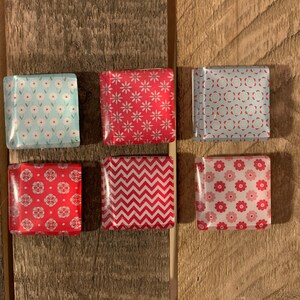 May include: Six square-shaped magnets with different patterns. The magnets are red, pink, and blue with white designs.