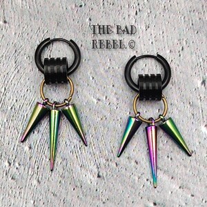 Può includere: Un paio di orecchini a cerchio neri con tre pendenti iridescenti a forma di cono. Gli orecchini hanno un design unico con una serie di anelli neri e anelli di collegamento color oro. Il testo "THE BAD REBEL" è visibile sullo sfondo.