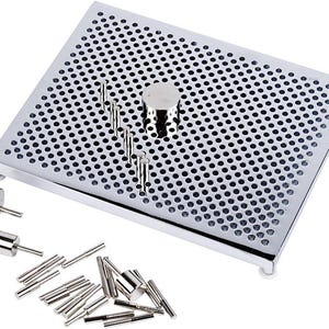 May include: A silver pegboard with many small holes, alongside various silver pegs and cylindrical pieces. The pegboard has a raised edge and is supported by small white feet. Some pegs are inserted into the board.