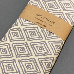 May include: A grey and white patterned wheat and lavender heat pack with the text "Meelie Moon Wheat & Lavender Bag Handmade" on a brown label.