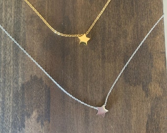 Puede incluir: Dos delicados collares con colgantes de estrella. El collar superior tiene un colgante de estrella dorada, y el collar inferior tiene un colgante de estrella plateada.