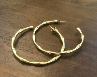 May include: A pair of gold hoop earrings with a bamboo-like design. The earrings are large and have a simple, elegant style.