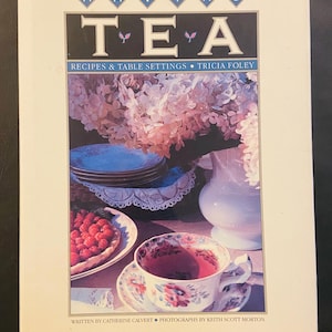 May include: A book cover titled "HAVING TEA" with the subtitle "RECIPES & TABLE SETTINGS." The cover features a photograph of a tea setting with a teacup, saucer, and a raspberry tart. The book is written by Catherine Calvert and photographed by Keith Scott Morton.