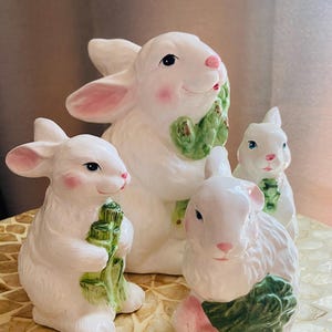 Può includere: Quattro statuette di coniglietti in ceramica bianca con accenti rosa sulle orecchie e sulle guance. Ogni coniglietto tiene in mano una verdura verde. I coniglietti variano in dimensioni e sono disposti insieme, creando un affascinante tema pasquale o primaverile.