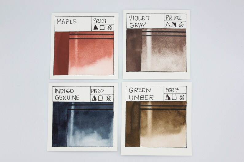 May include: Four watercolor paint swatches, each with a different color and pigment code. The colors are maple, violet gray, indigo genuine, and green umber.
