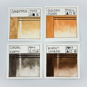May include: Four watercolor paint swatches on white paper. The swatches are labeled "Sandpiper PY43", "Golden Ochre PY42 H", "Cassel Earth PBK6", and "Burnt Umber PBR7".