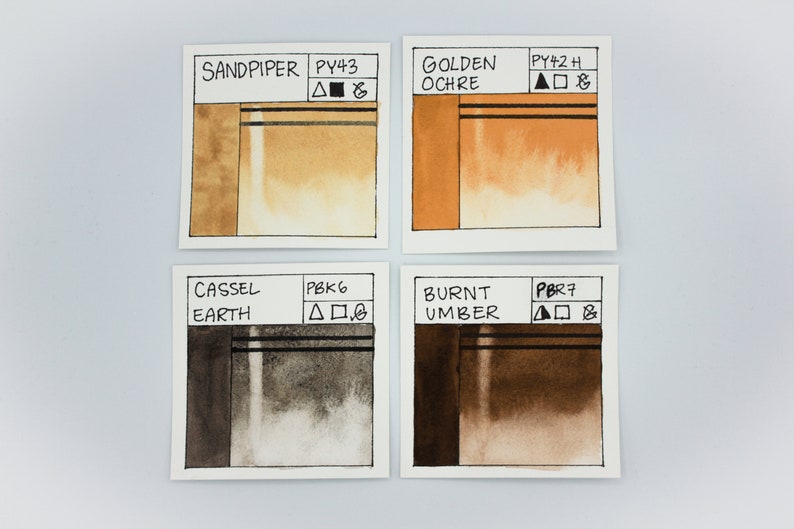 May include: Four watercolor paint swatches on white paper. The swatches are labeled "Sandpiper PY43", "Golden Ochre PY42 H", "Cassel Earth PBK6", and "Burnt Umber PBR7".