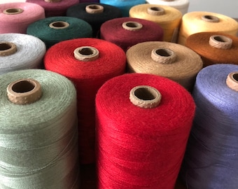 May include: A collection of spools of thread in various colors, including red, green, blue, brown, and beige. The spools are arranged in a triangular pattern.