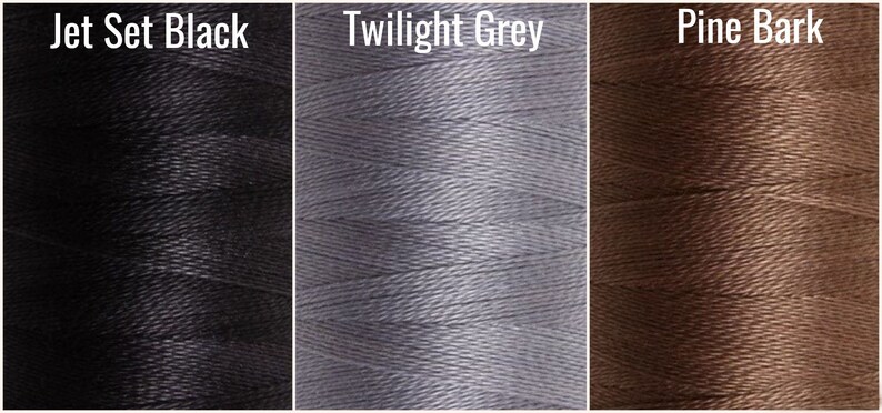 May include: Close-up of three spools of thread in the colors Jet Set Black, Twilight Grey, and Pine Bark.