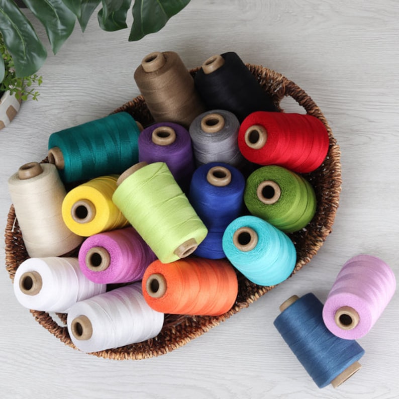 May include: A basket filled with spools of colorful thread in various shades of green, blue, red, yellow, purple, orange, white, and brown. The spools are arranged in a circular pattern, with the basket in the center.
