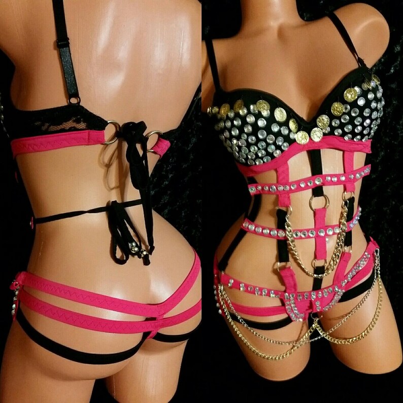 May include: A black and pink lingerie set with a bustier top featuring rhinestones and gold coins, and a harness with straps and chains.