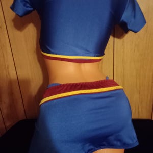 May include: A blue and maroon two-piece outfit with a short-sleeved crop top and a mini skirt. The skirt has a yellow stripe around the waistband.