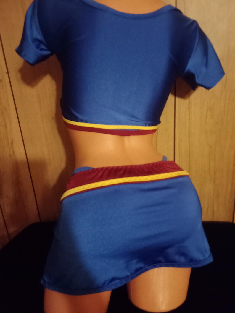 May include: A blue and maroon two-piece outfit with a short-sleeved crop top and a mini skirt. The skirt has a yellow stripe around the waistband.