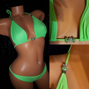 May include: A neon green bikini with silver and crystal embellishments. The top is a halter style and the bottom is a cheeky cut.