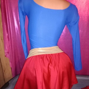May include: A red and blue costume with a gold belt. The top is a long-sleeved, blue shirt with a scoop neck. The skirt is a red, A-line skirt.