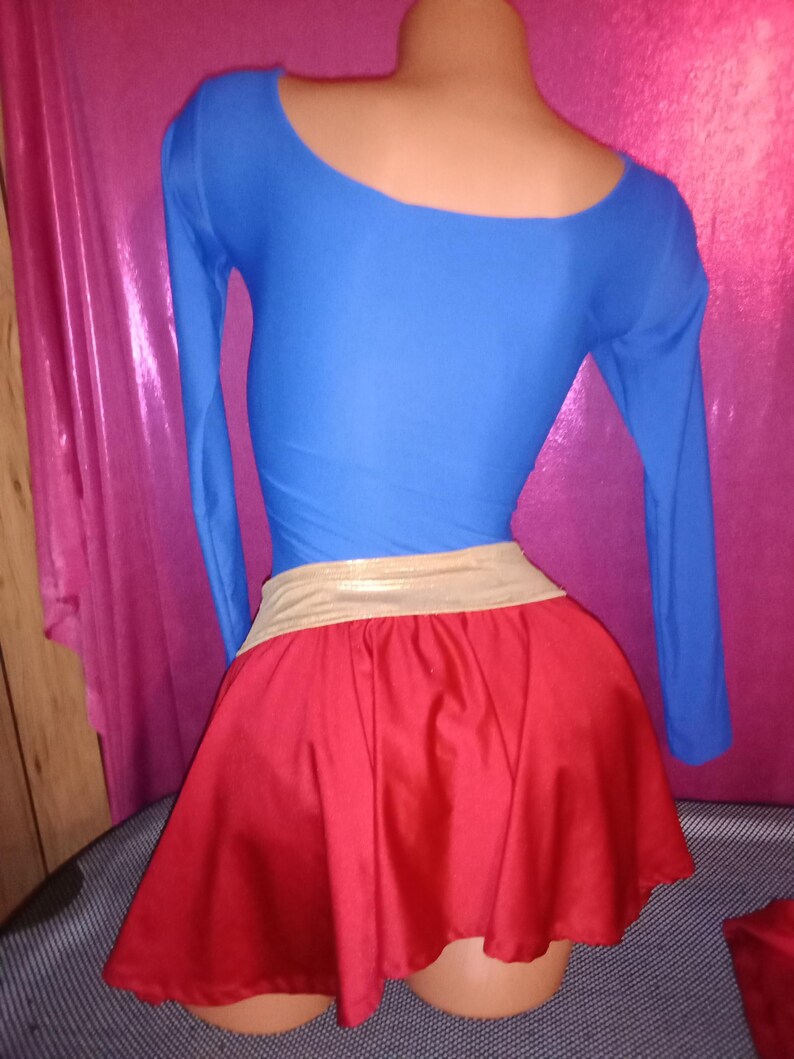 May include: A red and blue costume with a gold belt. The top is a long-sleeved, blue shirt with a scoop neck. The skirt is a red, A-line skirt.