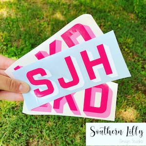May include: Three pink and white vinyl stickers with the letters S, J, and H in a 3D block style font. The stickers are on a white background.
