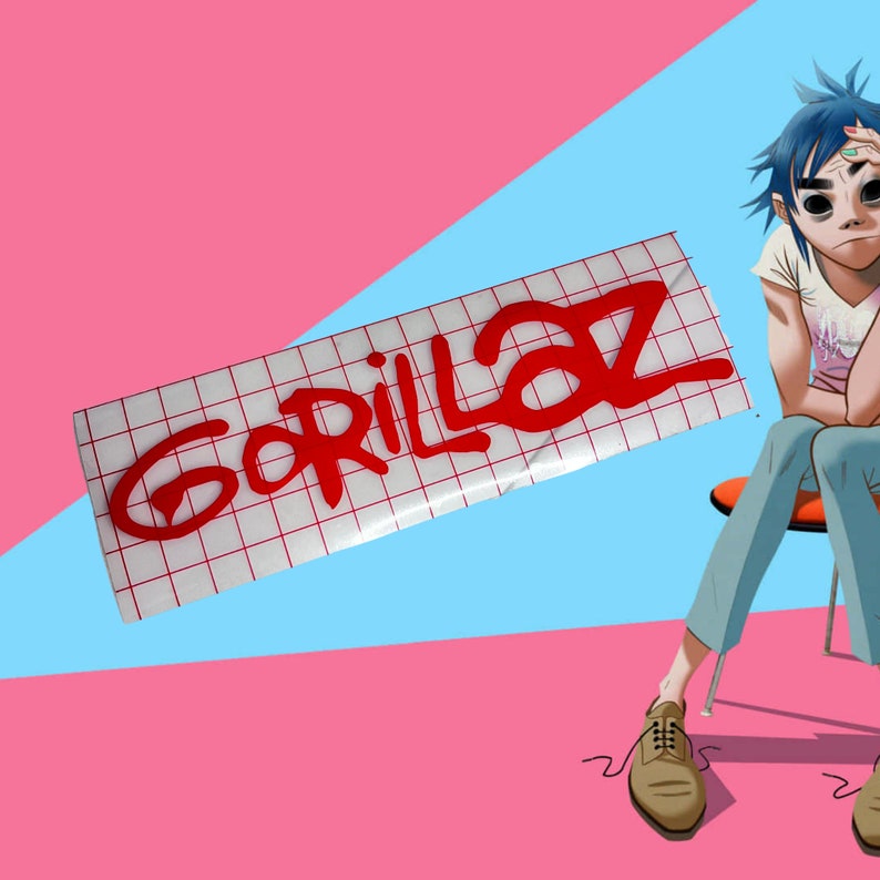 May include: A red "Gorillaz" sticker on a white grid background. The sticker is slightly angled and has a glossy finish.